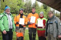 Mehrere Personen stehen vor einem Wald und blicken in Kamera